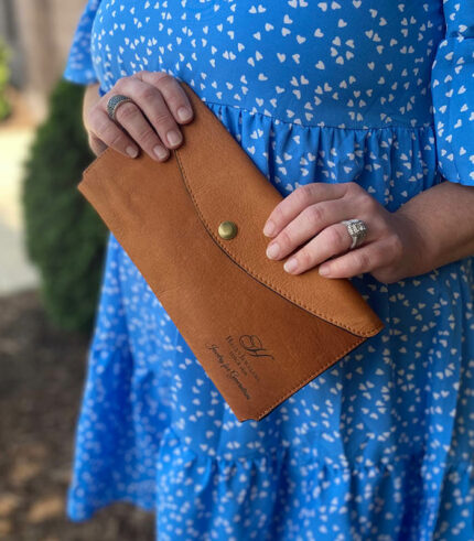 Small leather envelope being held by woman the front engraved with logo